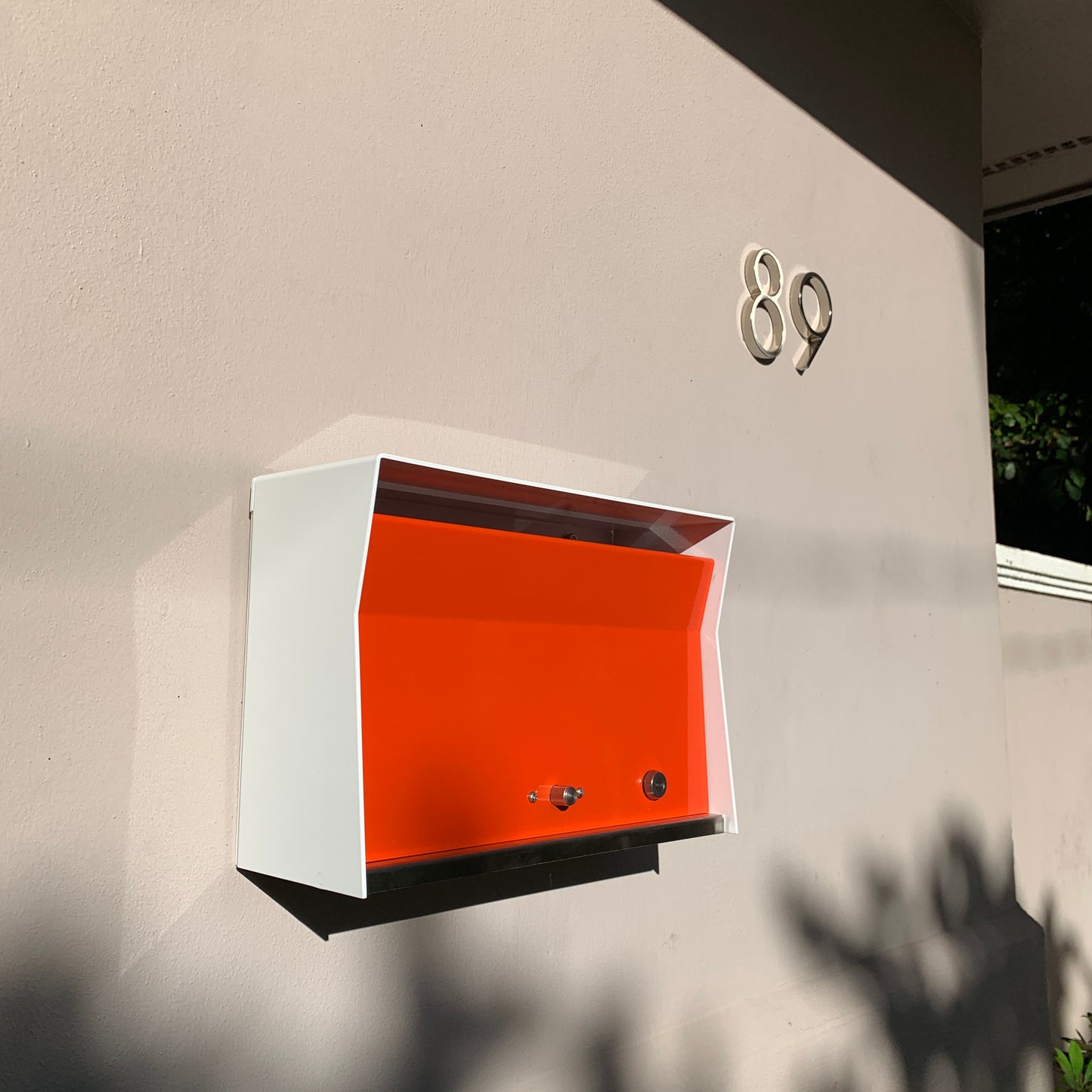 Wall Mount Mailbox mounted to outdoor wall. RetroBox in arctic white and orange
