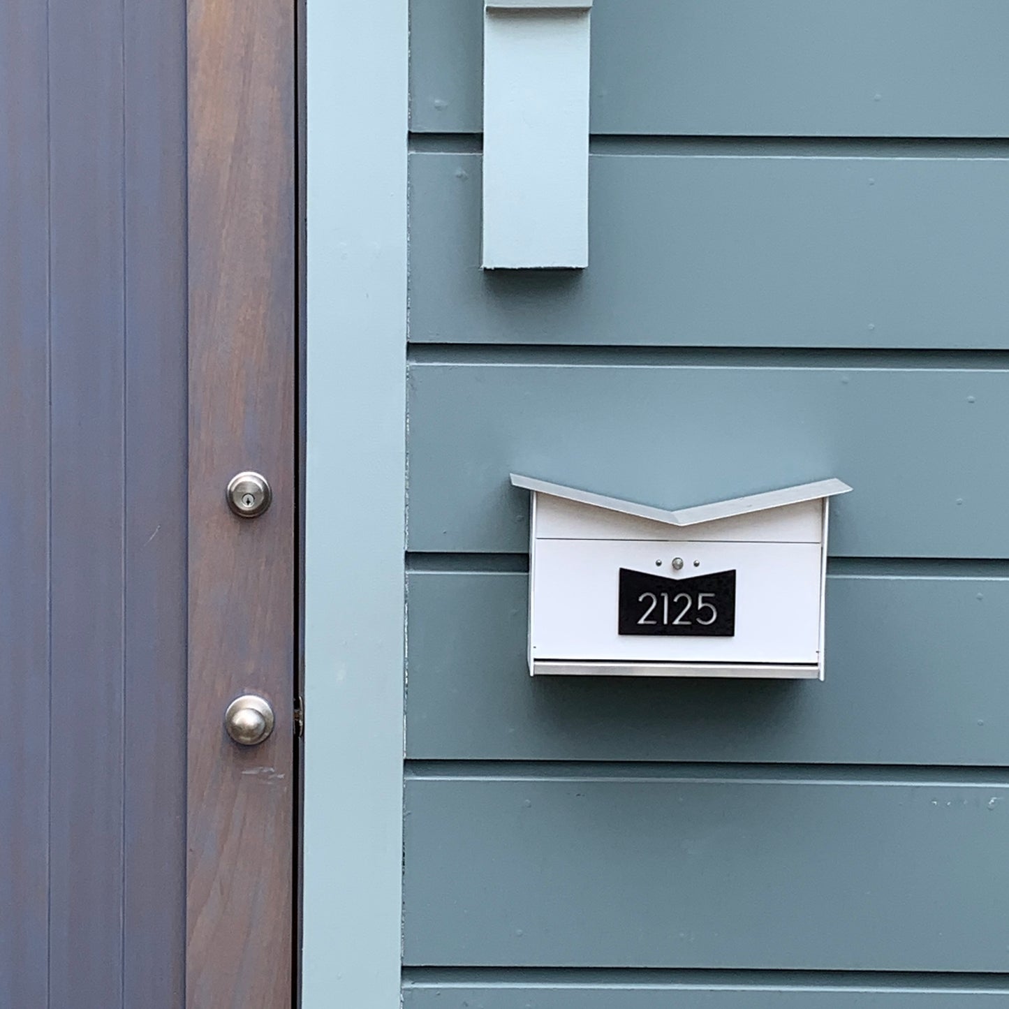 Wall Mount Mailbox mounted to outdoor wall panels. ButterFly Box in arctic white and jet black